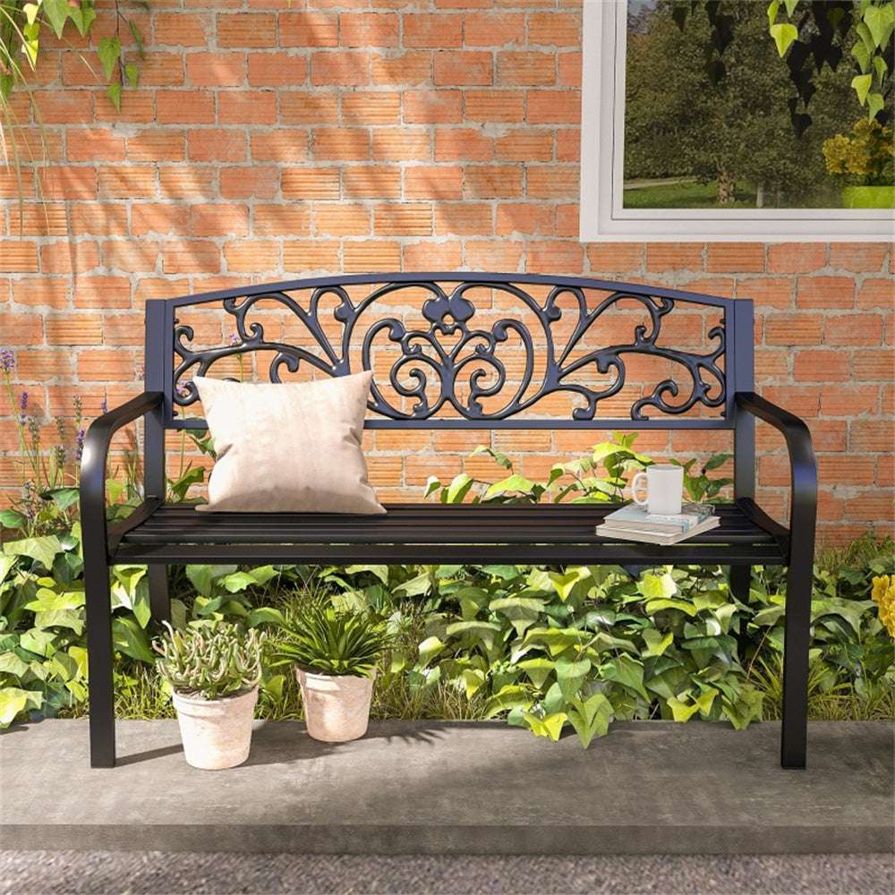 Decorative metal bench with a pillow and mug in a garden setting.