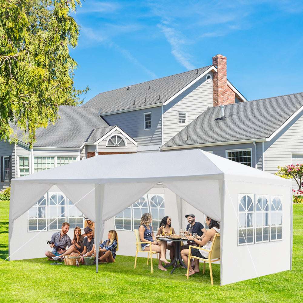 People sitting under a white outdoor canopy in a backyard with a house in the background.