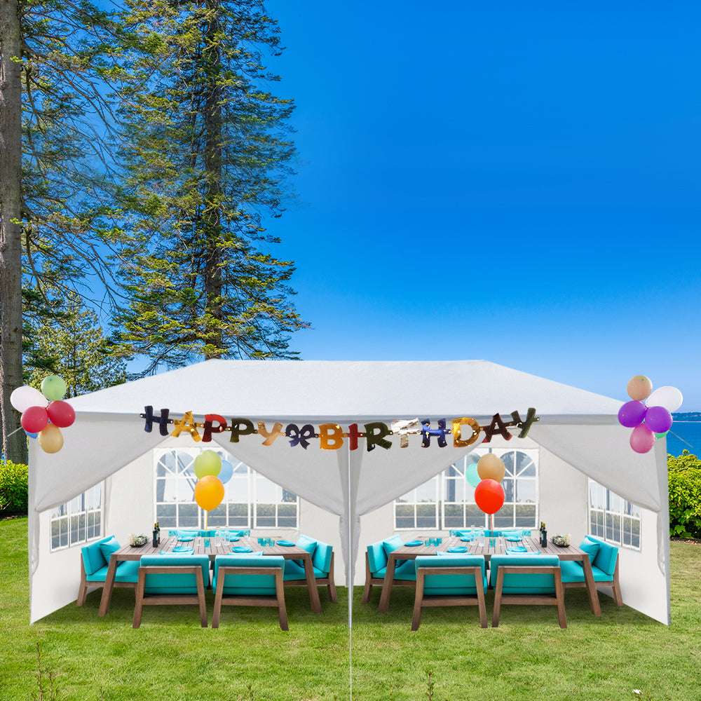 Outdoor birthday party setup with tables, chairs, and 'Happy Birthday' balloons under a white canopy.