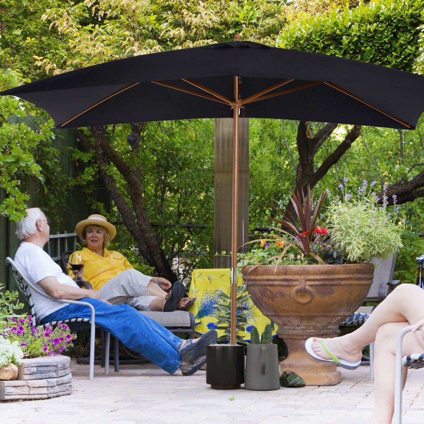 Two people sitting under a large black patio umbrella in a garden setting.