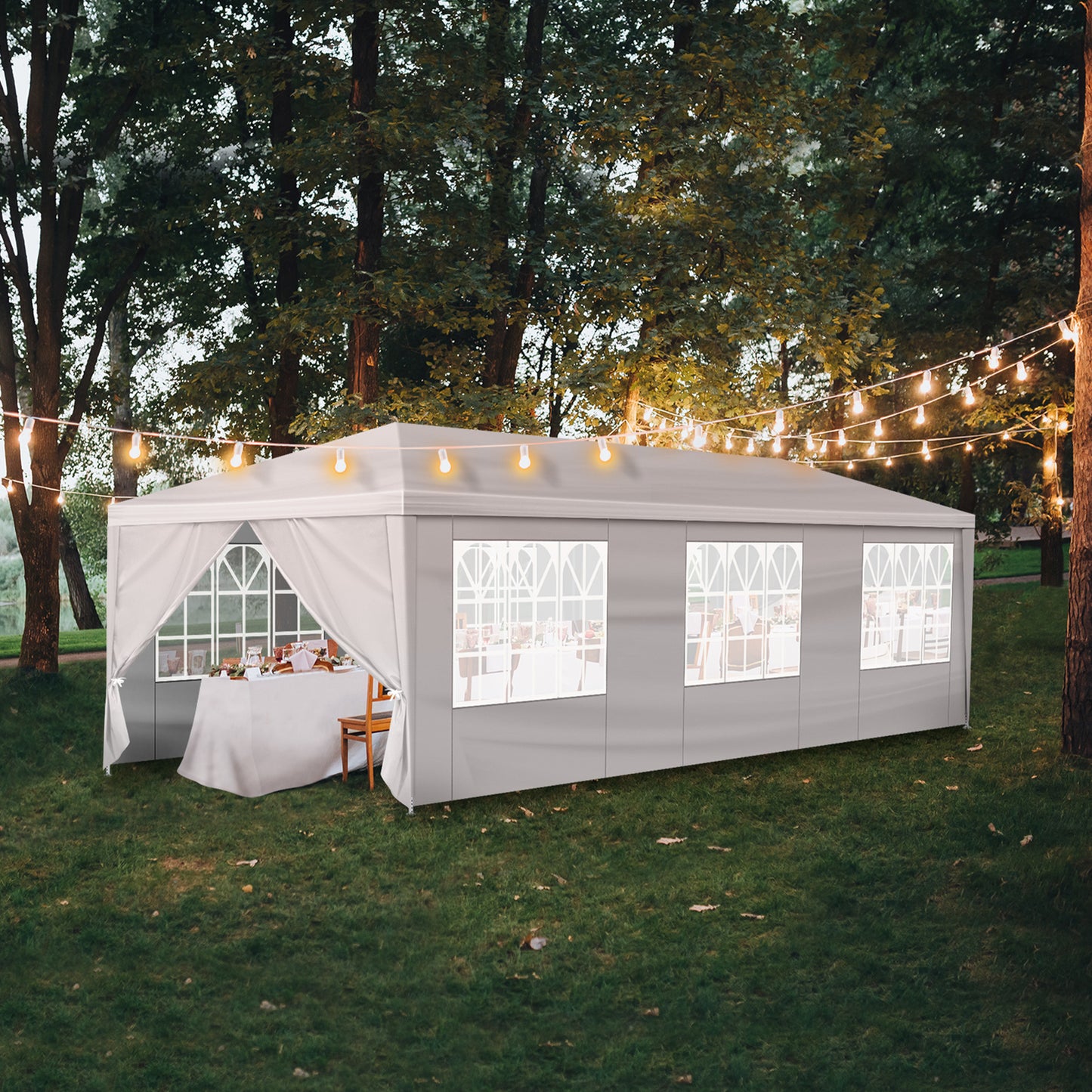 Outdoor event tent with string lights and a table inside, surrounded by trees.