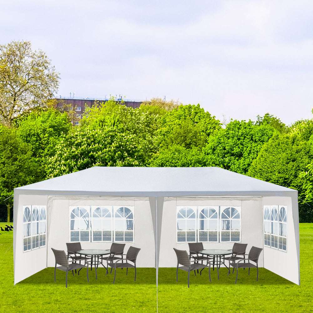 Outdoor gazebo with tables and chairs on a grassy area with trees in the background