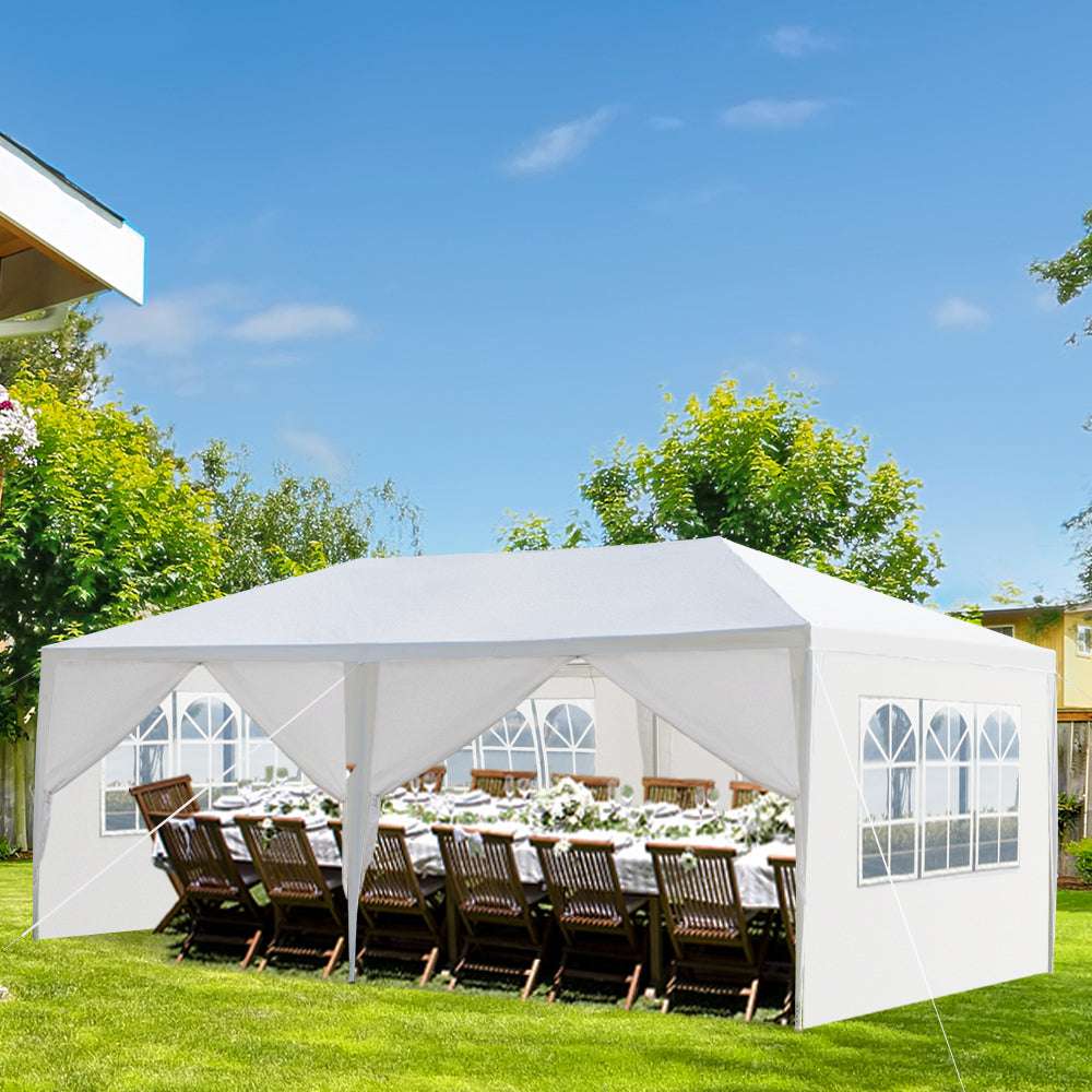 White outdoor canopy tent set up on a grassy area with tables and chairs underneath.