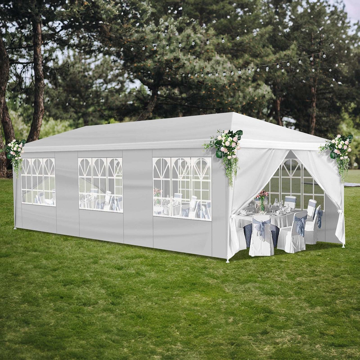 White outdoor party tent with tables and chairs set up on a grassy area with trees in the background.