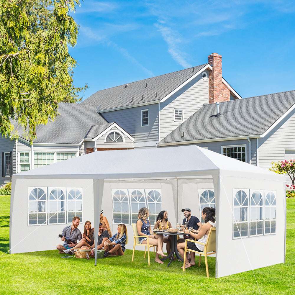 People sitting under a white outdoor canopy in a garden setting with a house in the background.