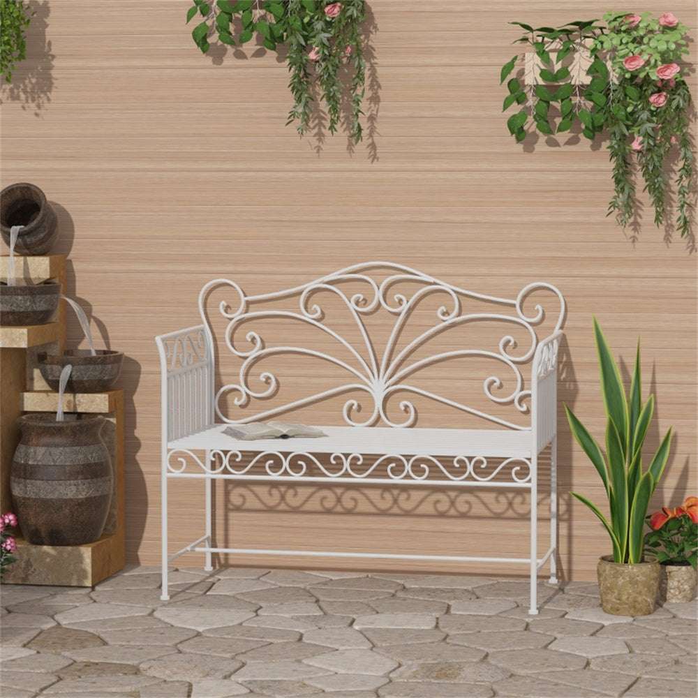 Decorative white metal bench in a garden setting with plants and a water feature.