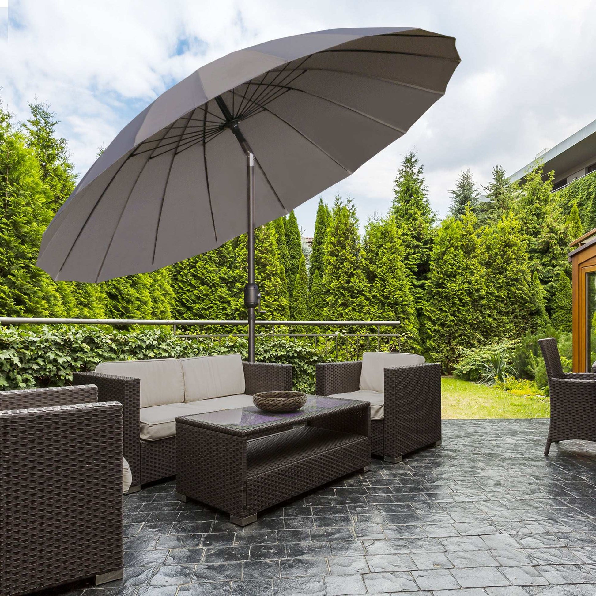 Outdoor patio set with a large umbrella on a stone patio, surrounded by greenery.
