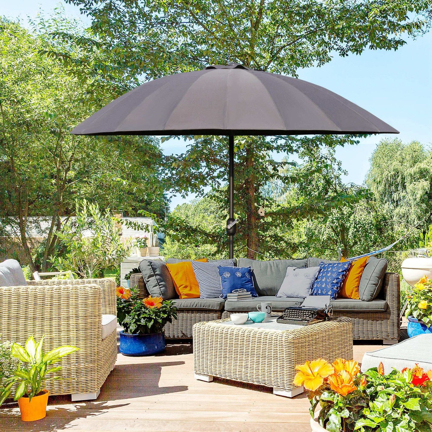 Outdoor patio with wicker furniture, cushions, and a large umbrella on a sunny day.