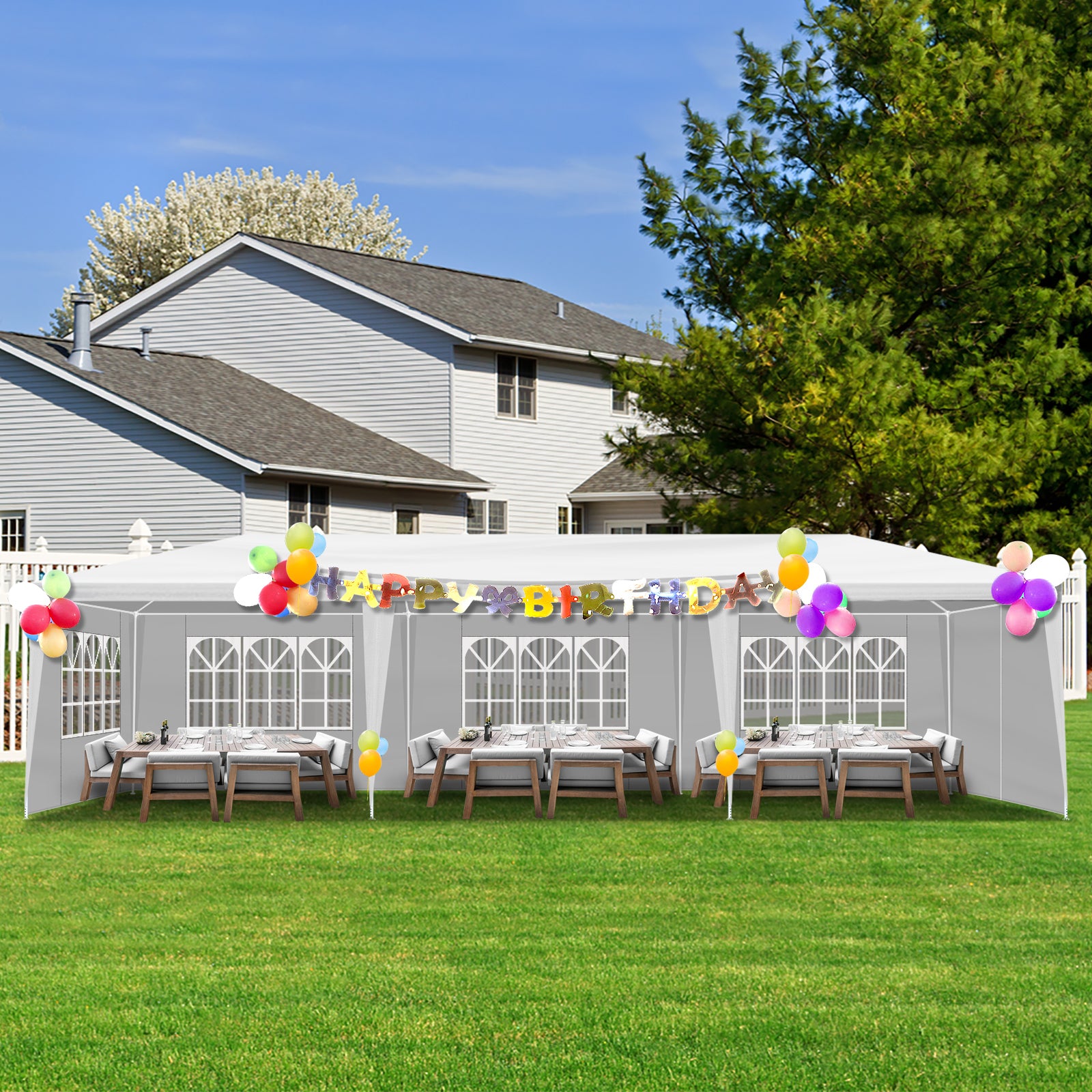 Outdoor birthday party setup with a tent, tables, chairs, and balloons in front of a house.