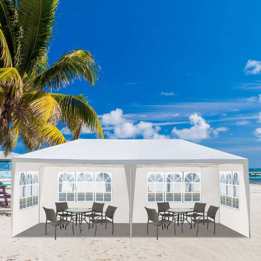 White outdoor canopy tent with tables and chairs on a beach with palm trees and blue sky.