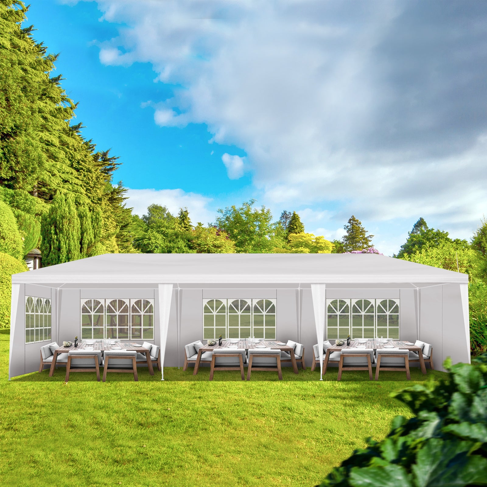 White outdoor party tent with tables and chairs set up on a grassy area with trees in the background.