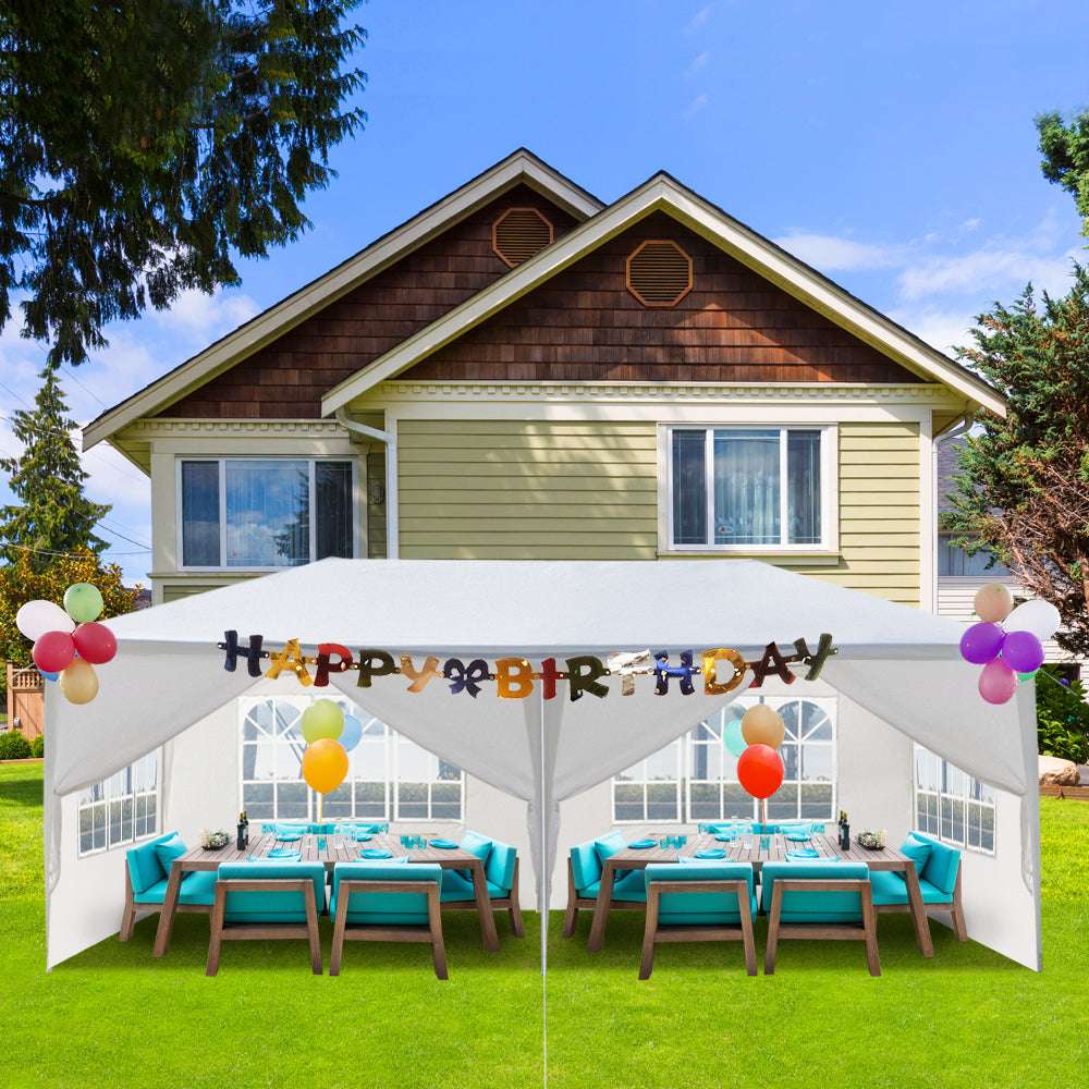 Outdoor birthday party setup with a canopy, tables, chairs, and balloons in front of a house.