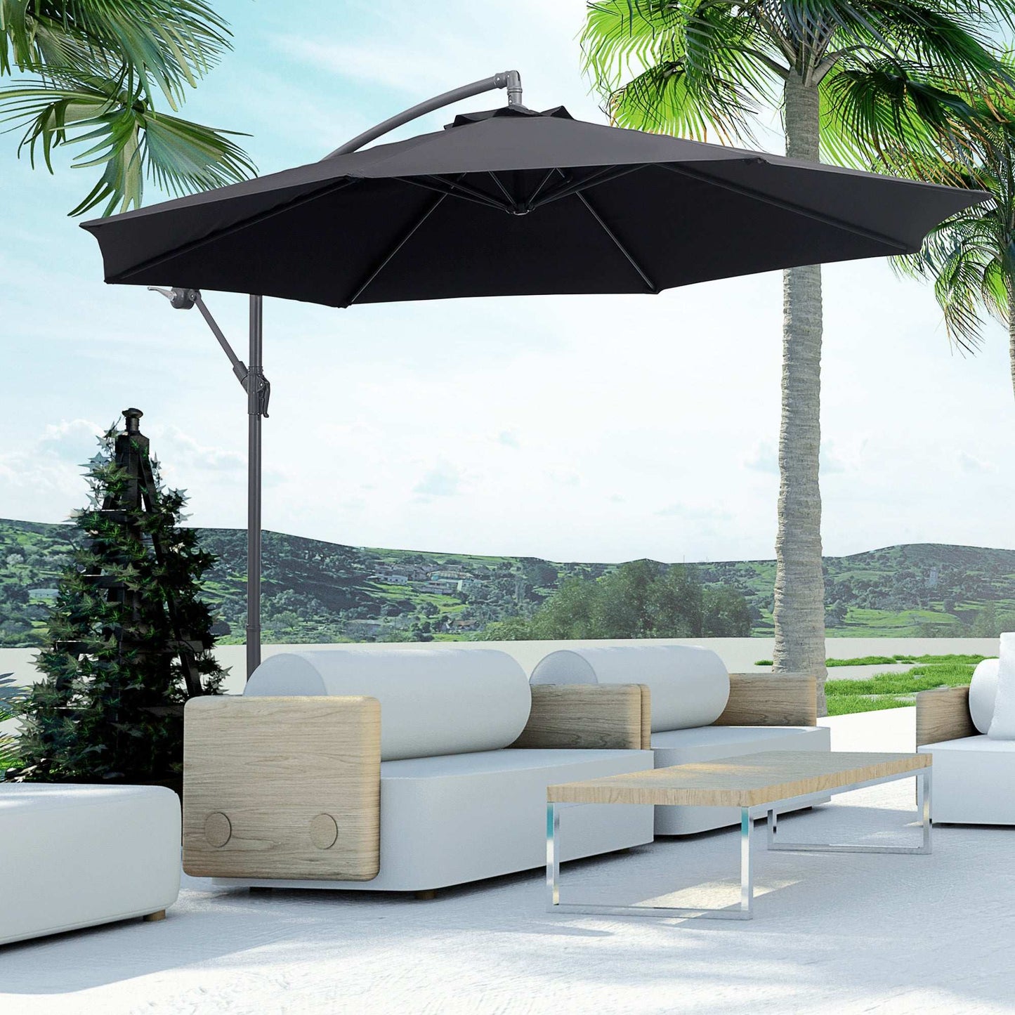 Outdoor patio with a large black umbrella, white sofa, and wooden coffee table against a scenic background.