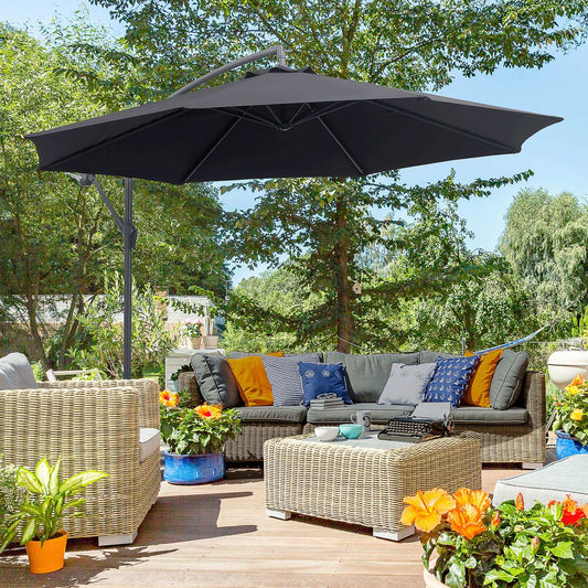 Outdoor patio with wicker furniture, cushions, and a large black umbrella under trees.