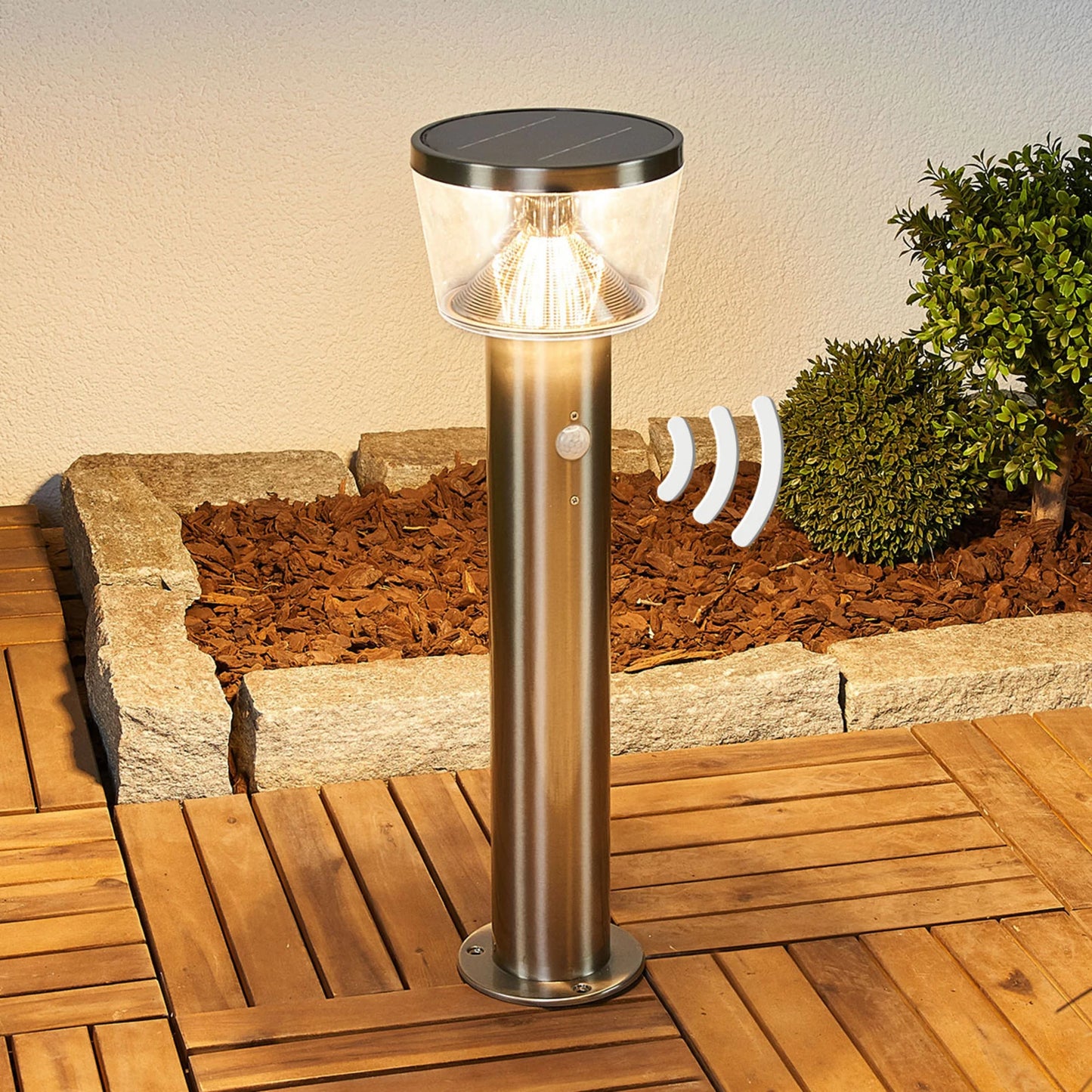 Solar-powered stainless steel pedestal light illuminating a modern garden path at dusk
