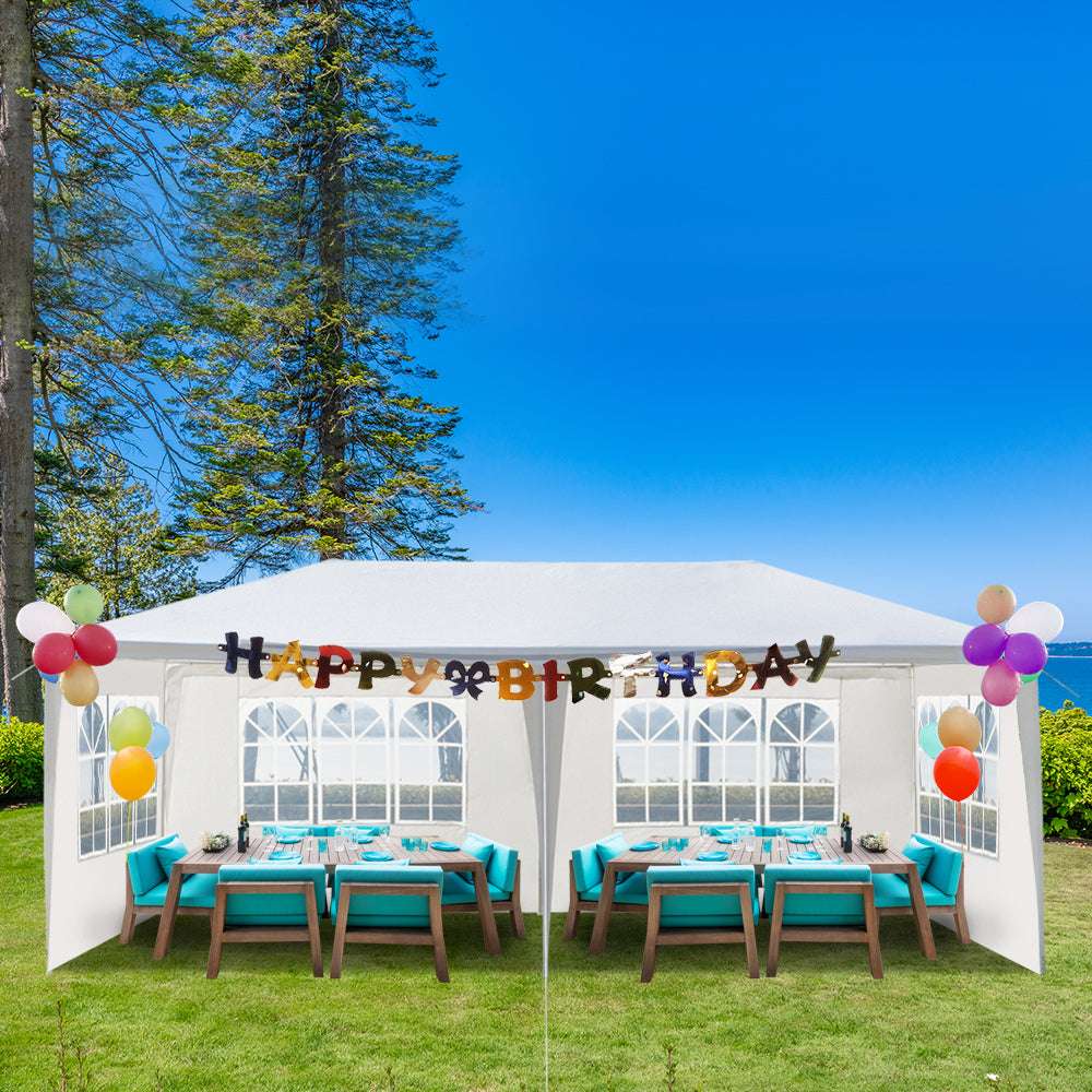 Outdoor birthday party setup with tables, chairs, and 'Happy Birthday' balloons in a garden.