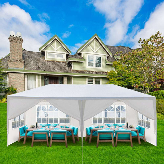 White outdoor canopy tent set up on a grassy area in front of a house with tables and chairs underneath.