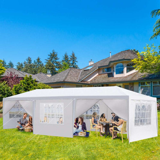 White outdoor canopy tent with people sitting inside on a sunny day.