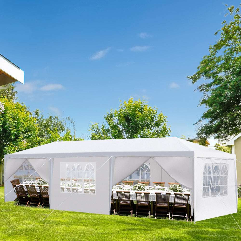 White outdoor canopy tent set up on a grassy area with tables and chairs underneath.