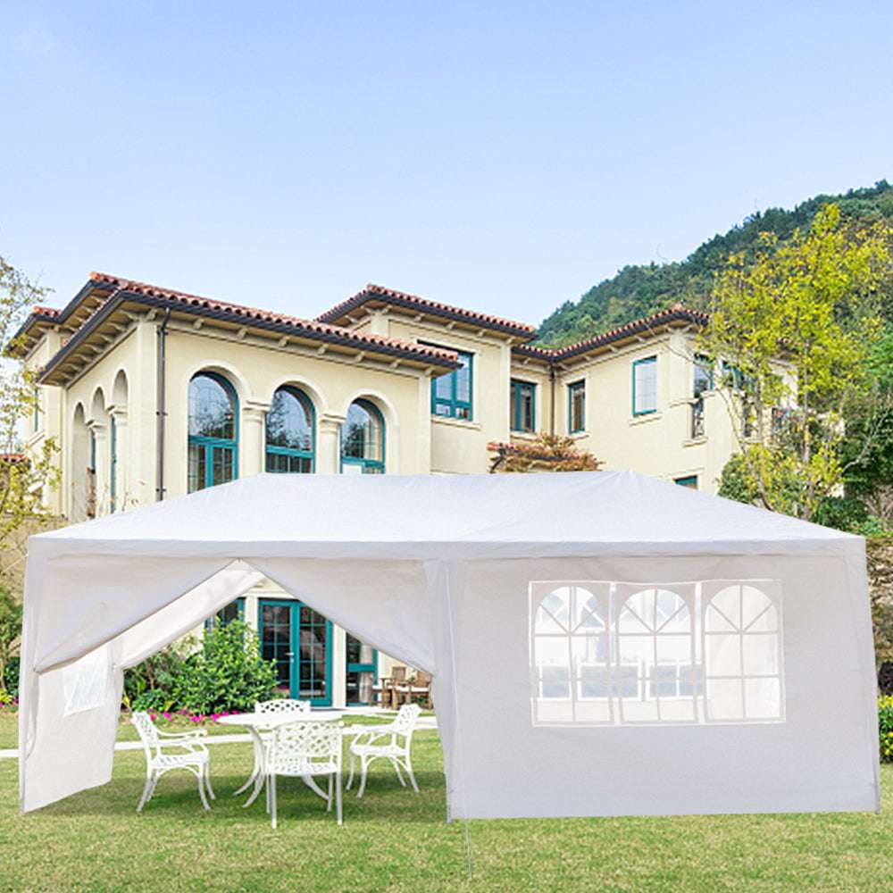White outdoor canopy tent set up on a lawn in front of a large house with mountains in the background.