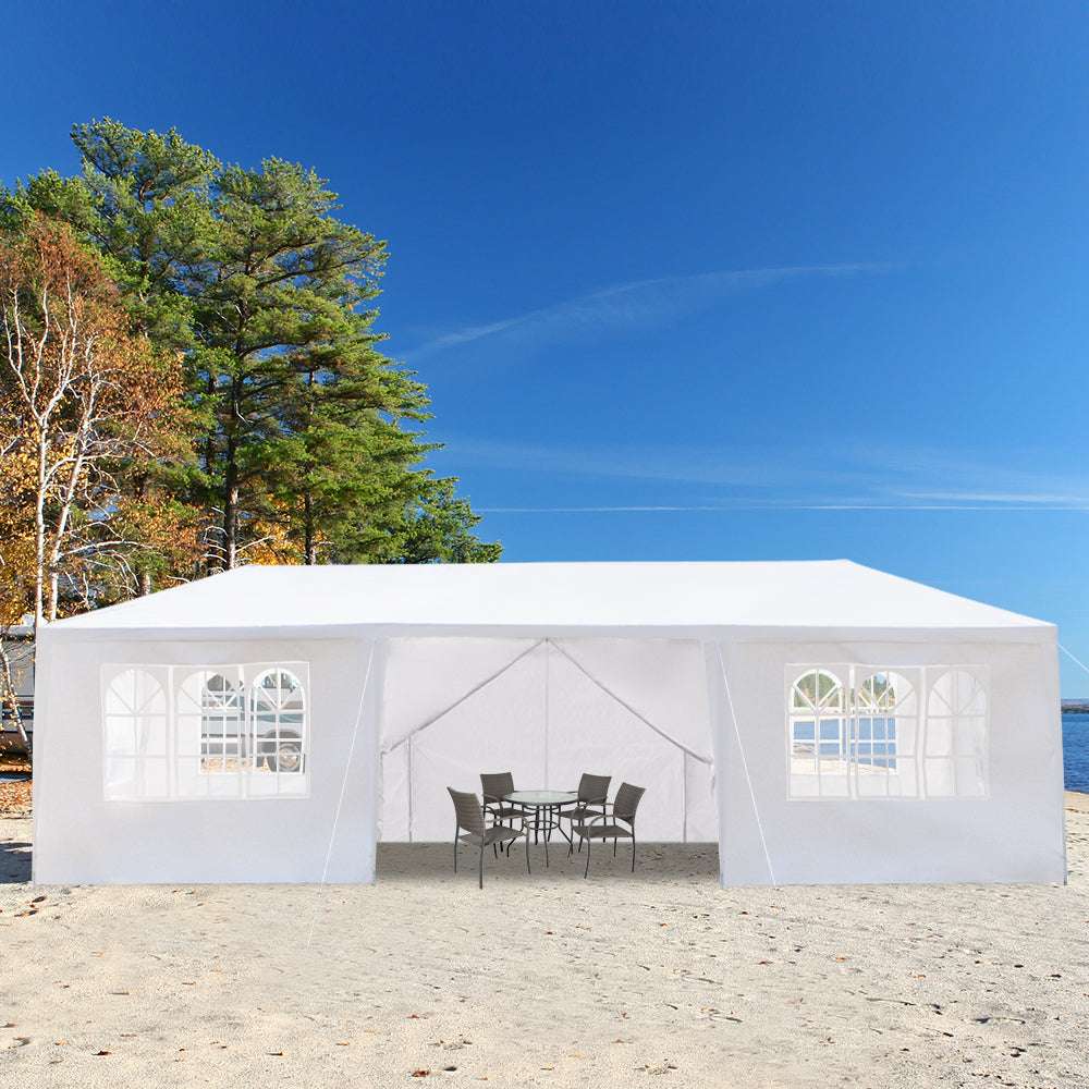 White outdoor canopy tent with windows on a sandy beach with trees and blue sky.