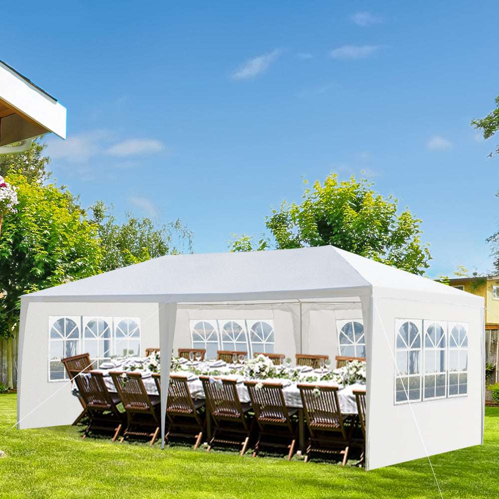 White party tent set up outdoors with a table and chairs under a clear blue sky.