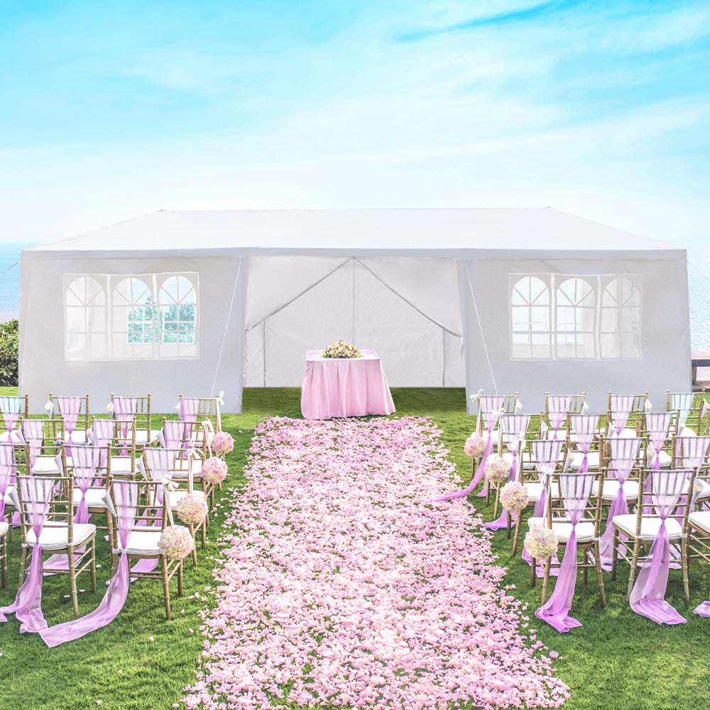 Decorated outdoor event space with pink chairs, tablecloth, and flower petals on a grassy area.