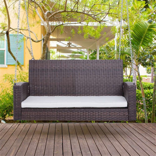 Wicker swing chair with a cushion on a wooden deck in a garden setting.