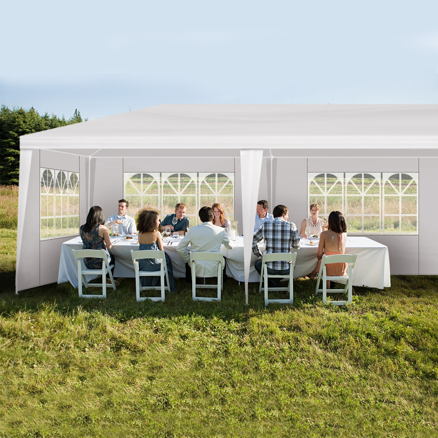 People sitting at tables under a large white outdoor tent in a grassy area.
