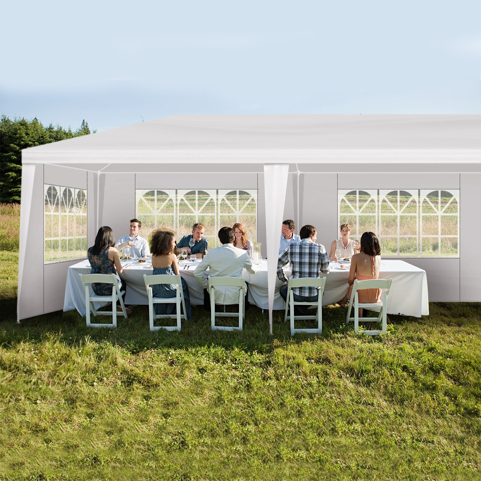 People sitting at tables under a large white outdoor tent in a grassy area.