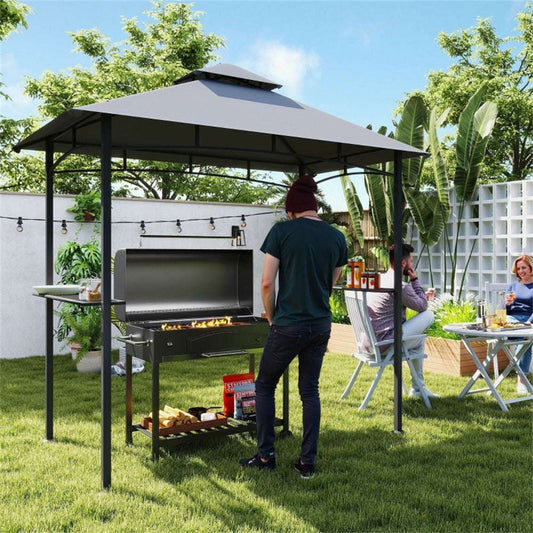 People grilling outdoors under a gazebo in a backyard setting.